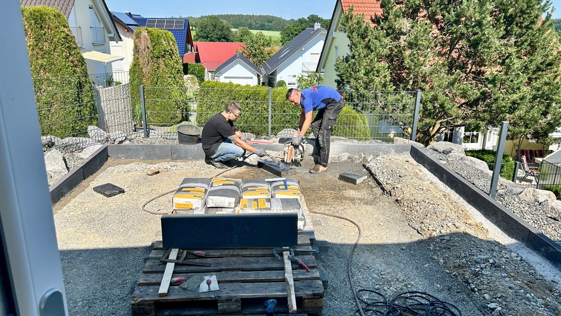 Zwei Mitarbeiter schneiden Pflastersteine beim Bau einer Einfahrt mit Unterbau.