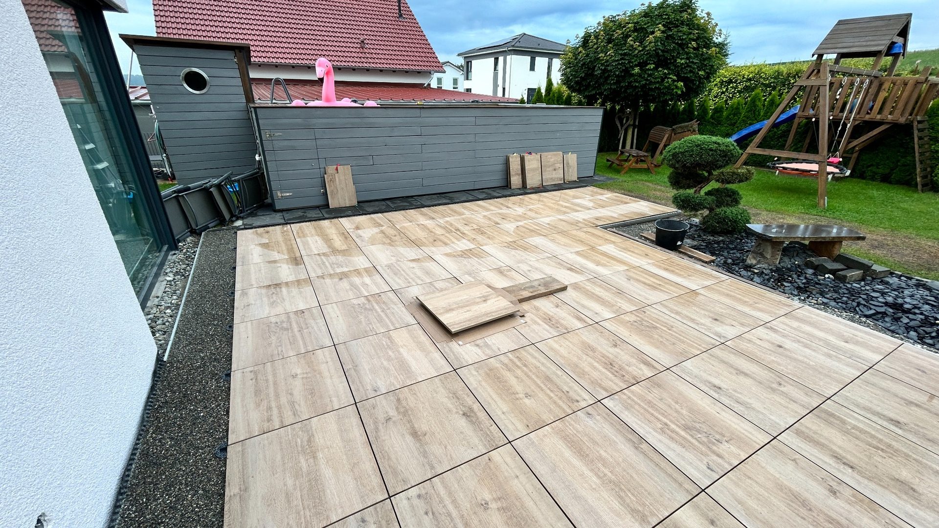 Großformatige Terrassenplatten in Holzoptik werden auf einer Terrasse verlegt.
