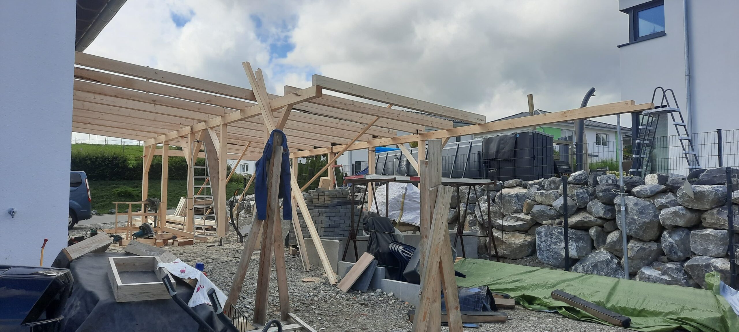Holz-Carport in der Bauphase mit sichtbarer Rahmenkonstruktion neben einem Wohnhaus.
